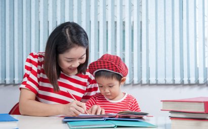 Cute boy doing his school homework with his mother, at home, he Asian cute boy doing his school homework with his mother, at home, he is writing on a book